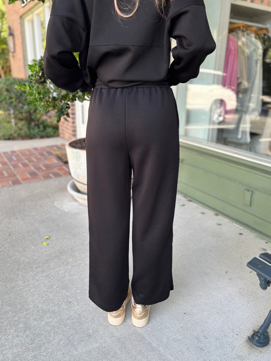 Person wearing a black outfit with wide-leg pants standing on a sidewalk.