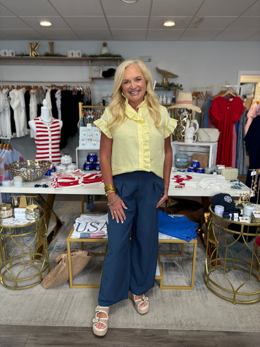 Woman in a yellow shirt and blue pants standing in a store with various items on display.