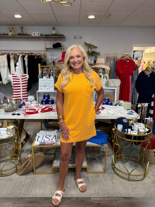 Woman in a yellow dress standing in a store with various items on display.