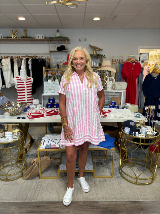 Woman in a pink and white striped dress standing in a store with various items on display.
