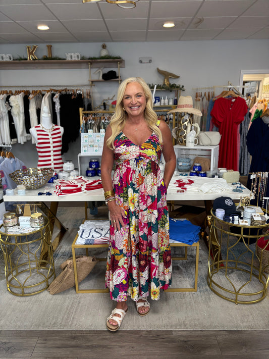 Woman in a colorful dress standing in a store with clothing and decor items around her.