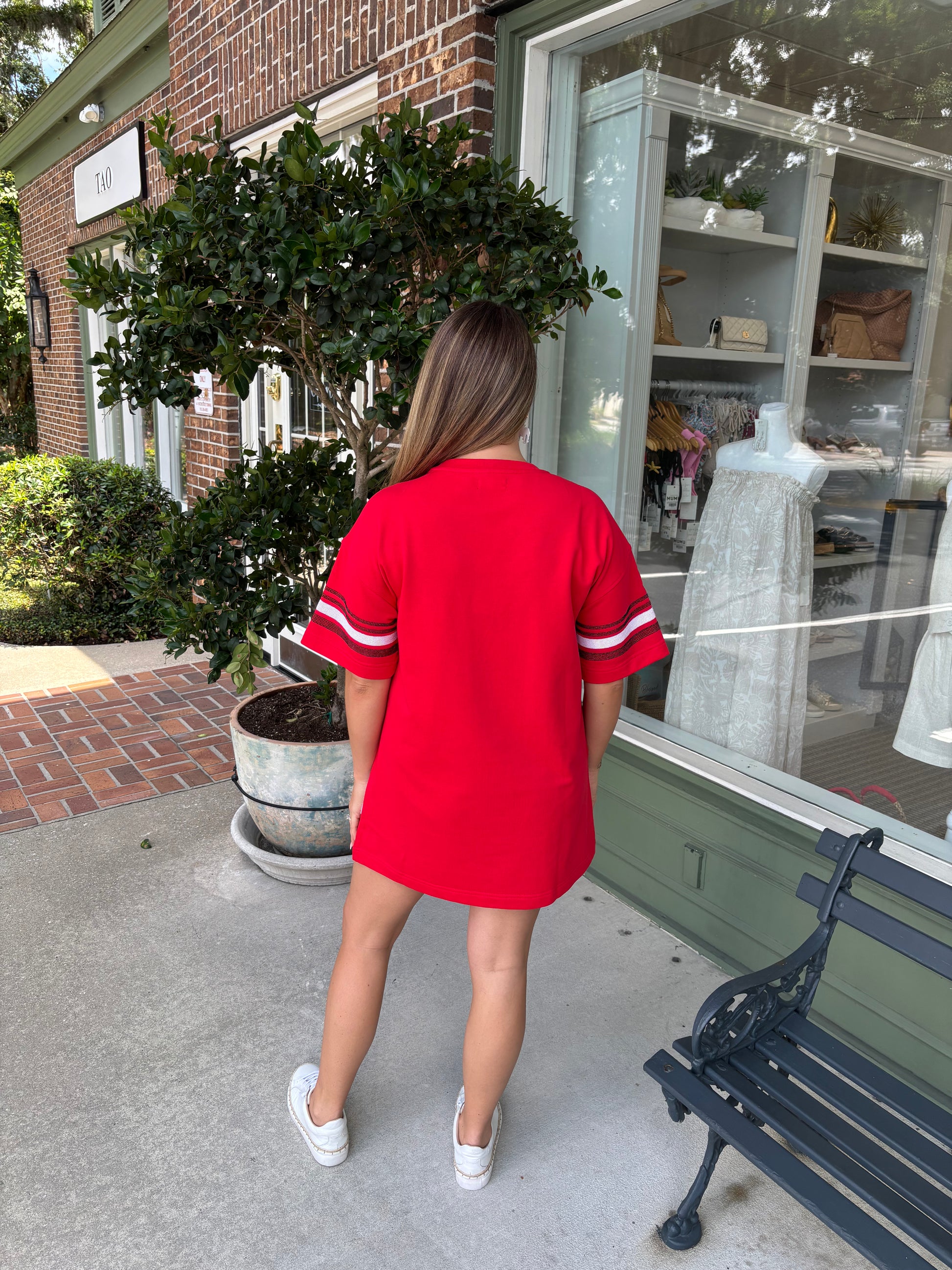 Person wearing a red dress with white stripes standing outside a store.