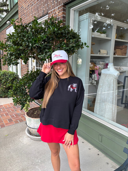Woman wearing a black sweatshirt with a bulldog logo and a red skirt, standing outside a store.