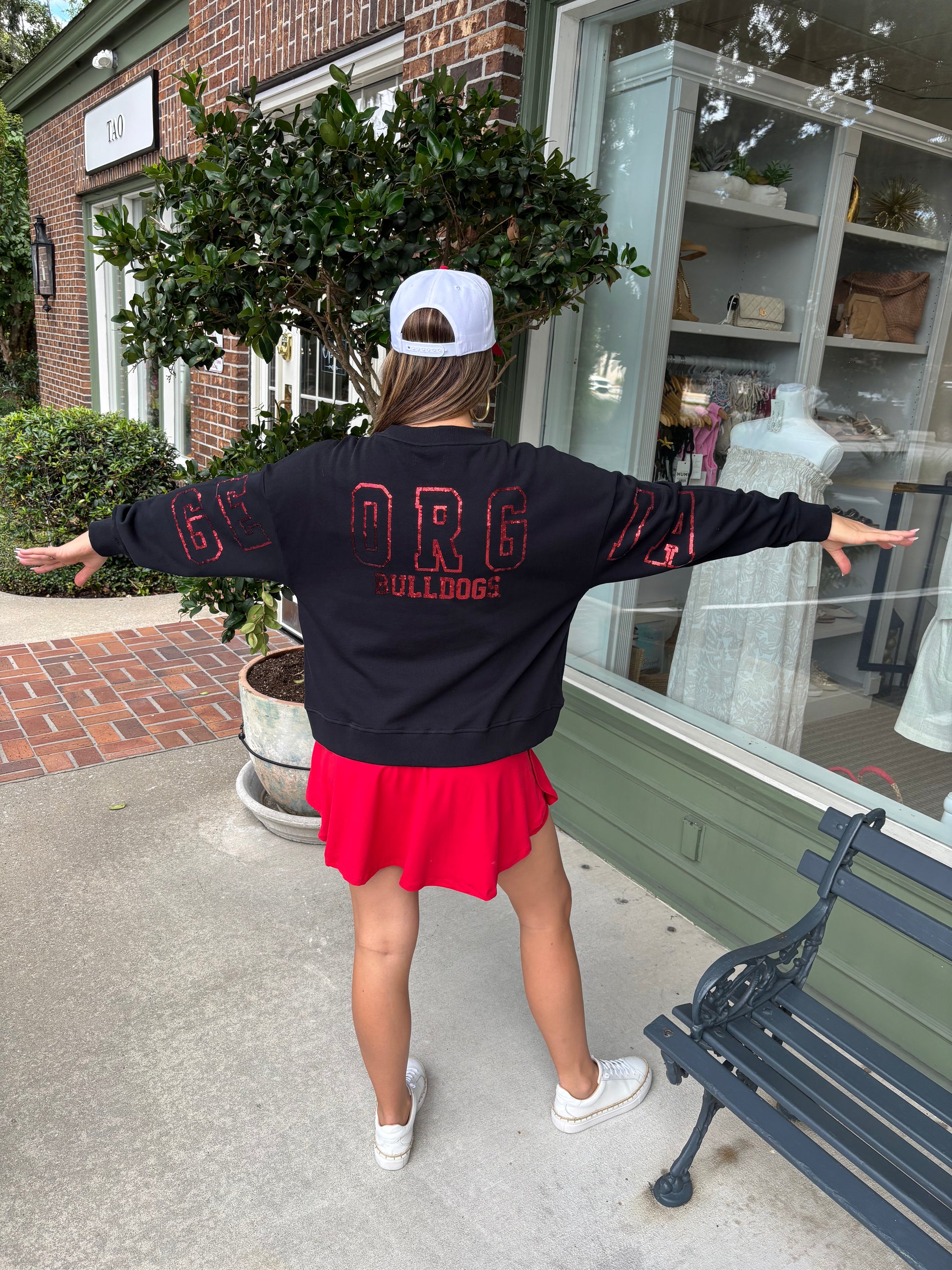 Person wearing a black sweatshirt with red text and a red skirt, standing in front of a store.