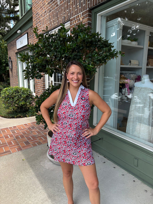 Woman in a red floral dress standing outside a store with brick walls and greenery.