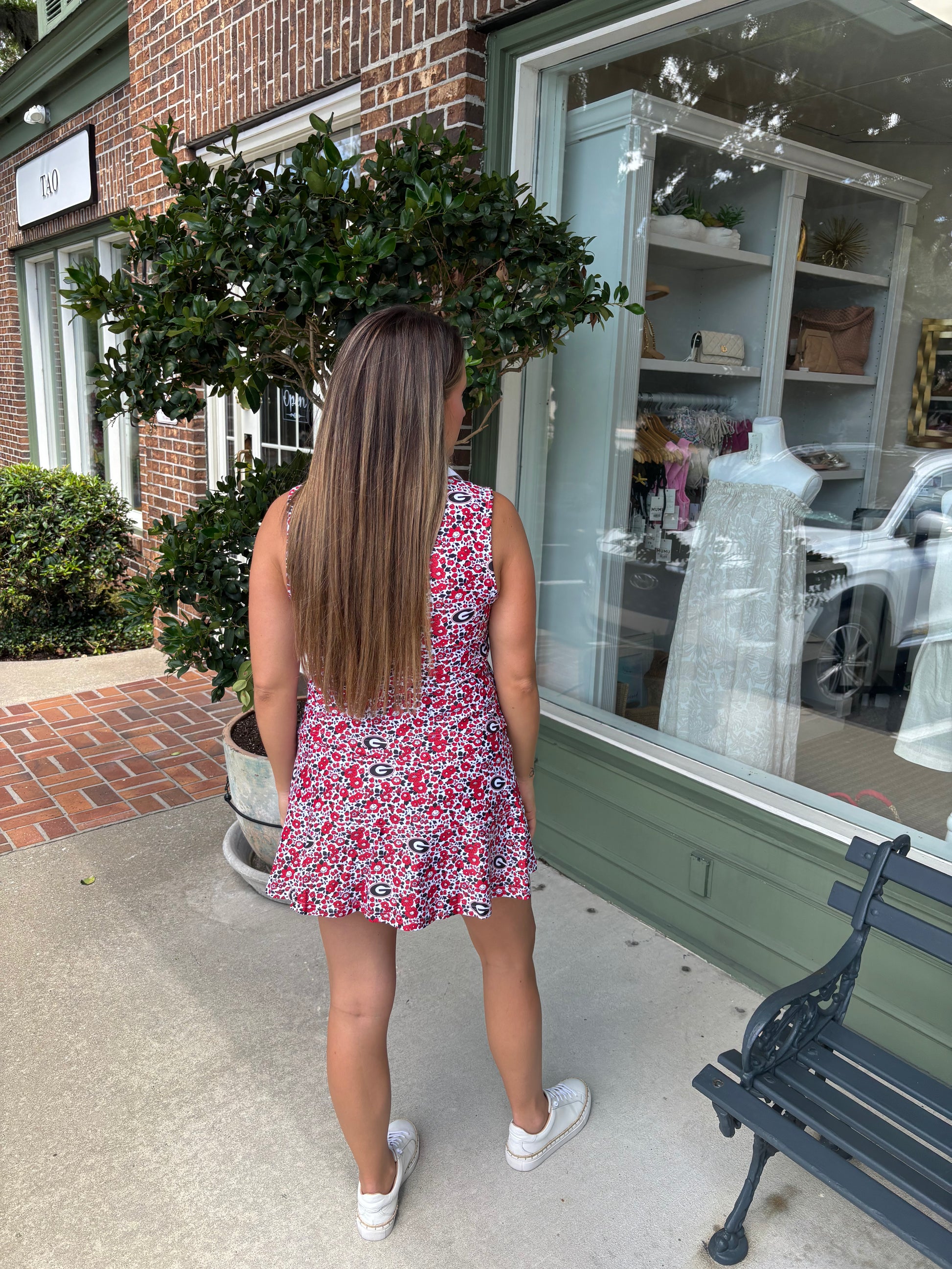 Woman in a floral dress standing outside a store with a bench and plant in the foreground.