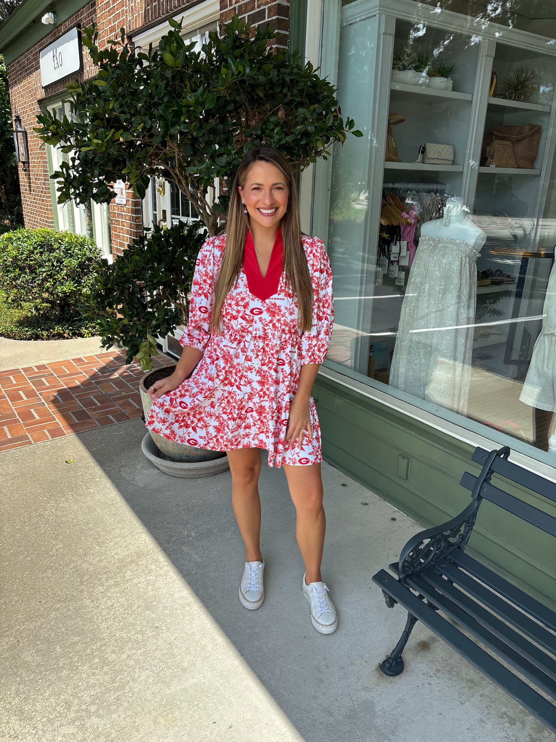 Woman in a red floral dress standing outside a store with a window display.