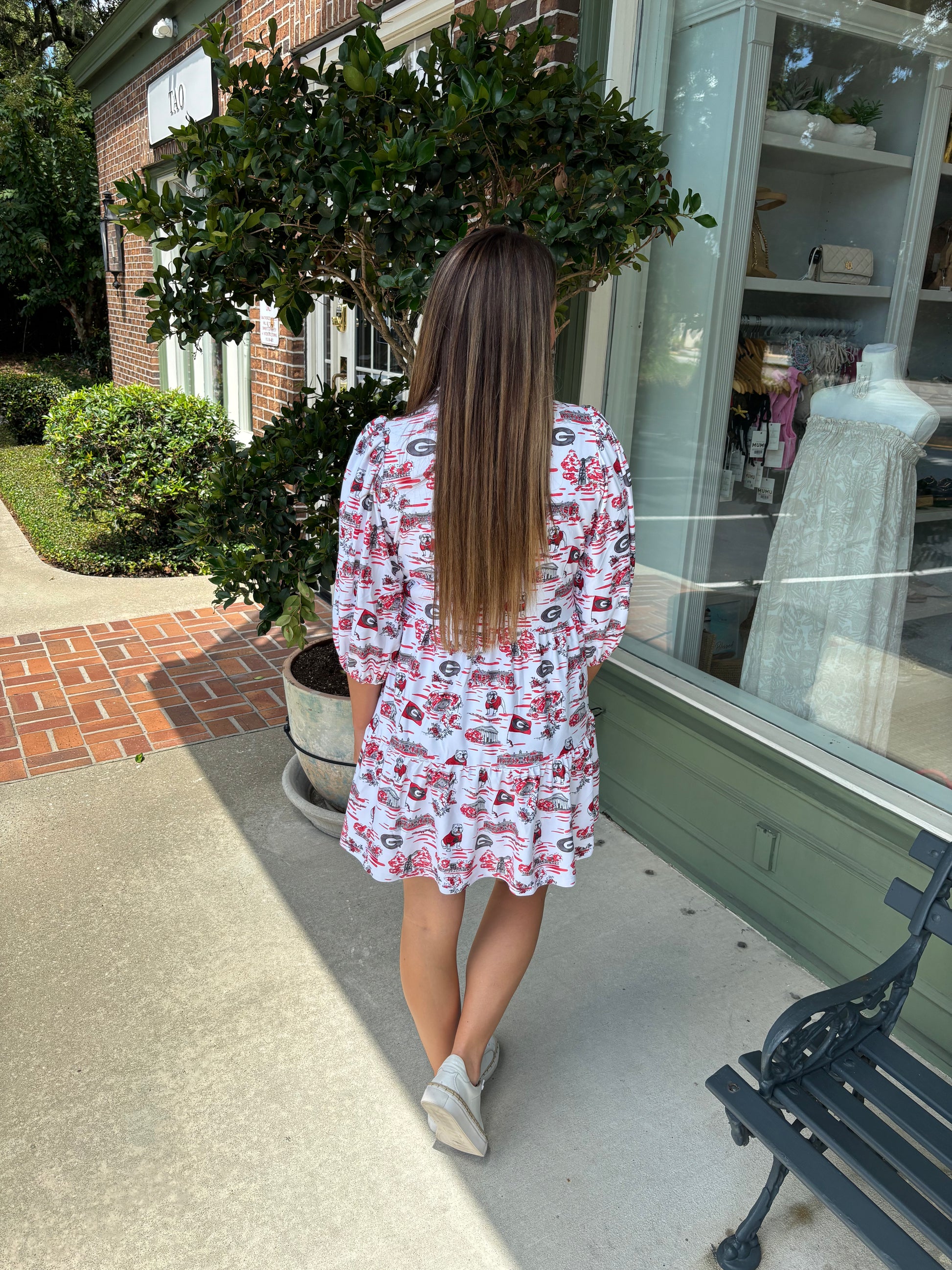 Woman in a patterned dress walking on a sidewalk near a store window.