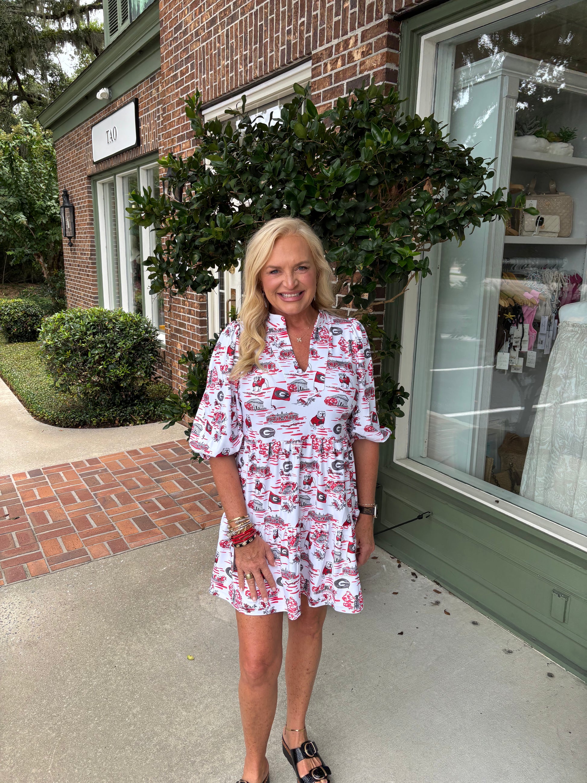 Woman in a patterned dress standing outside a building with a window display.