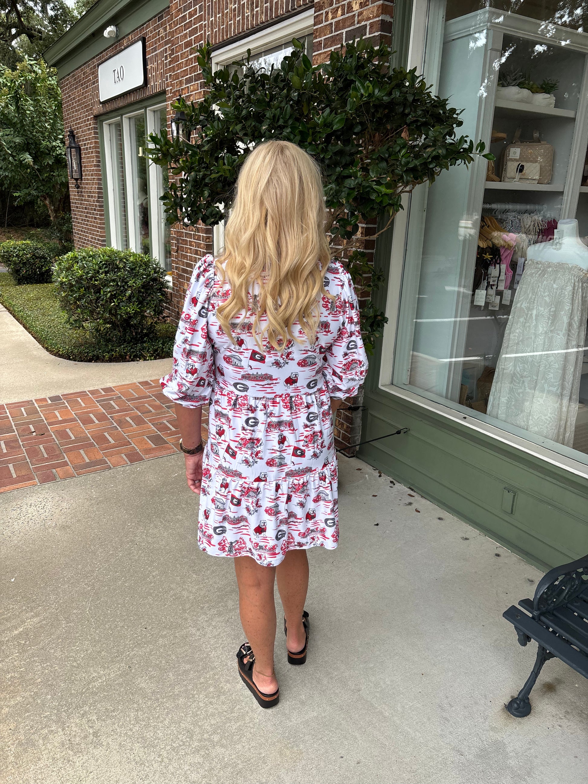 Woman in a patterned dress walking outside a store with a brick facade.
