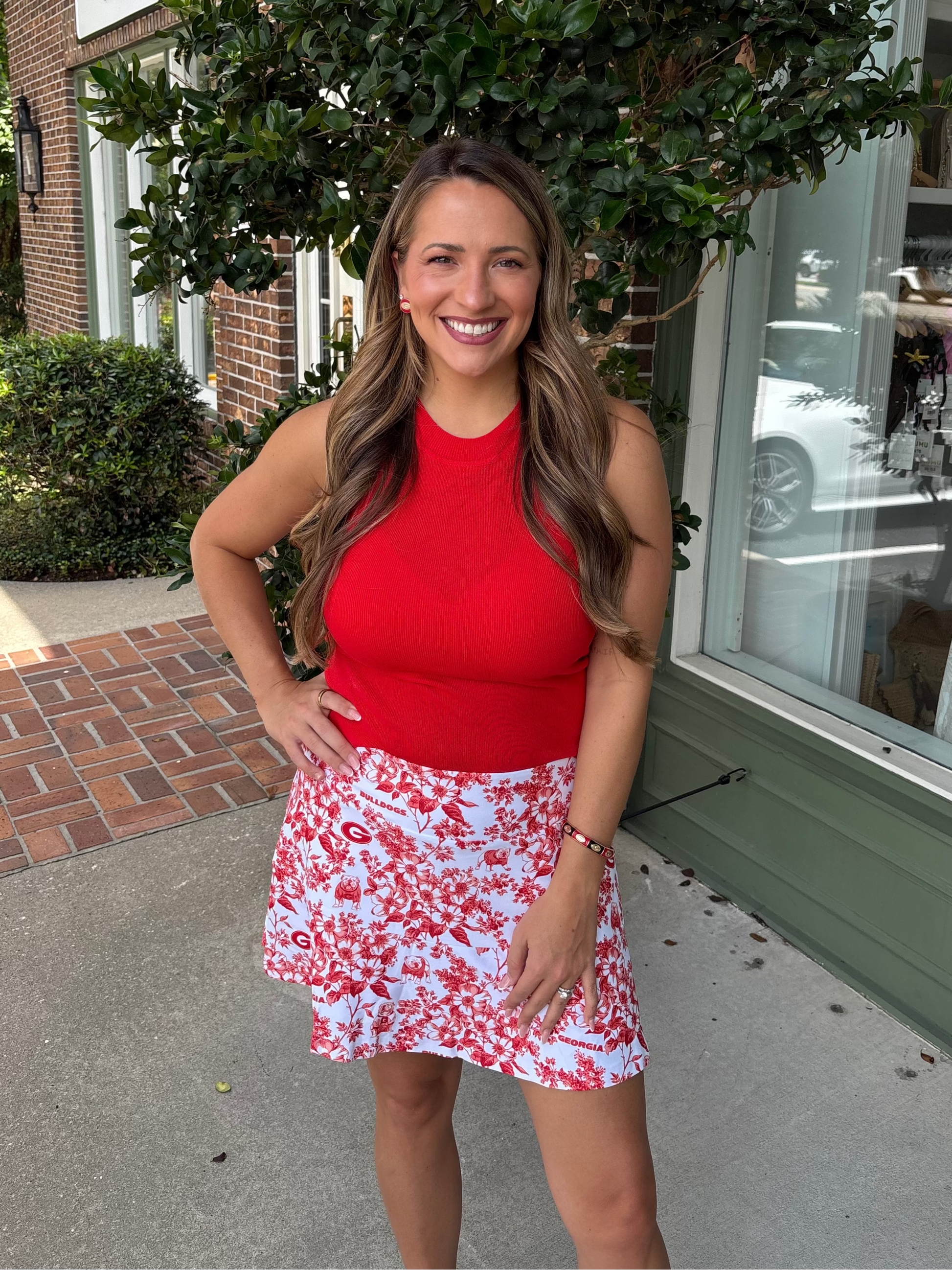 Woman wearing a red top and floral skirt standing outdoors.