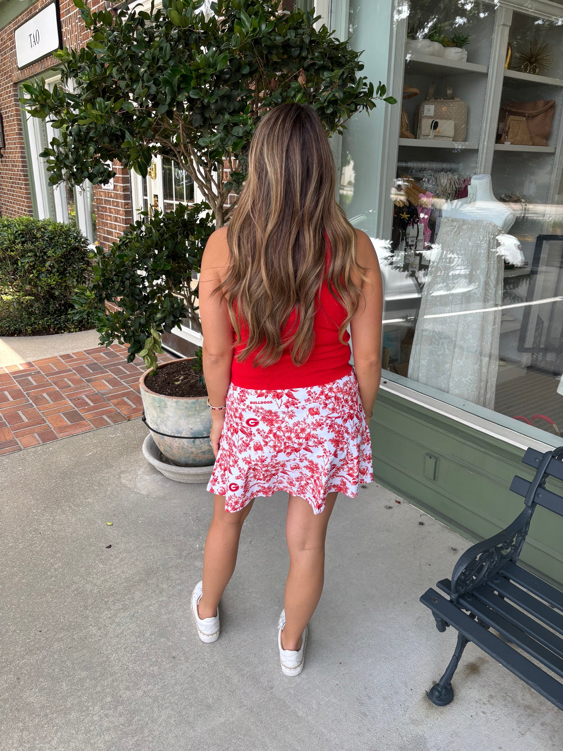 Person wearing a red top and white floral skirt with red patterns outdoors.