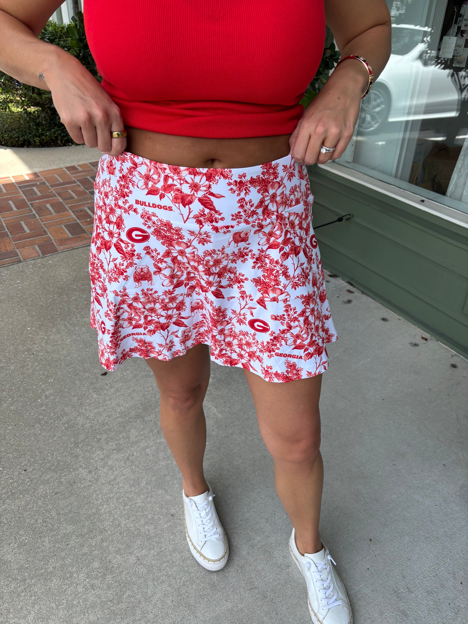 Person wearing a red floral skirt with white sneakers on a concrete surface.