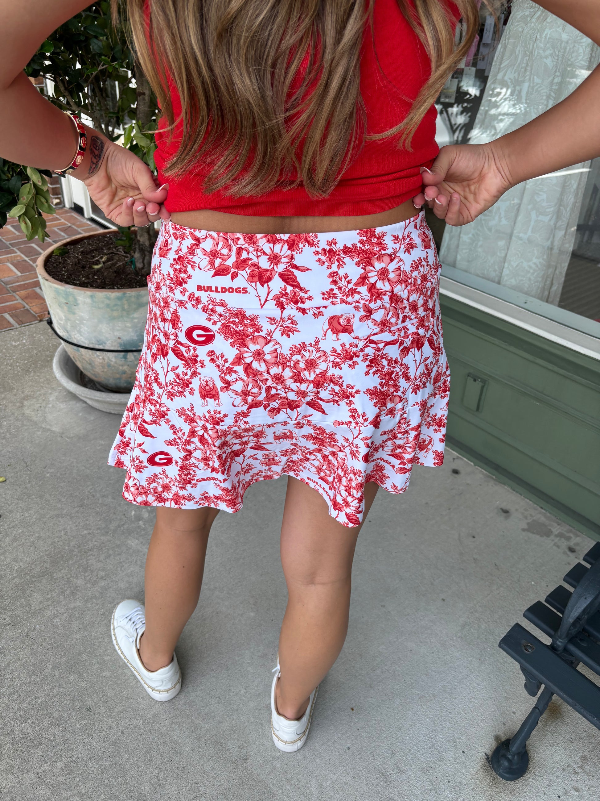 Person wearing a red top and white floral skirt with red patterns outdoors.