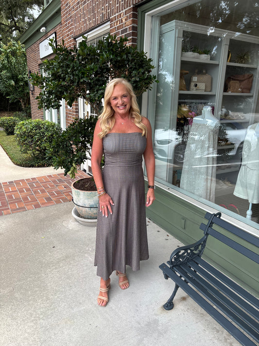 Woman in a gray dress standing outside a store with a bench and plants in the background.
