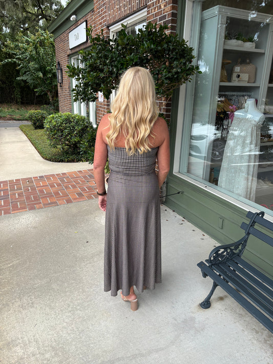 Woman in a long dress standing outside a store with a bench and window display.