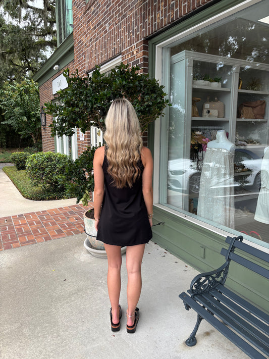 Woman in a black dress standing on a sidewalk next to a store window.