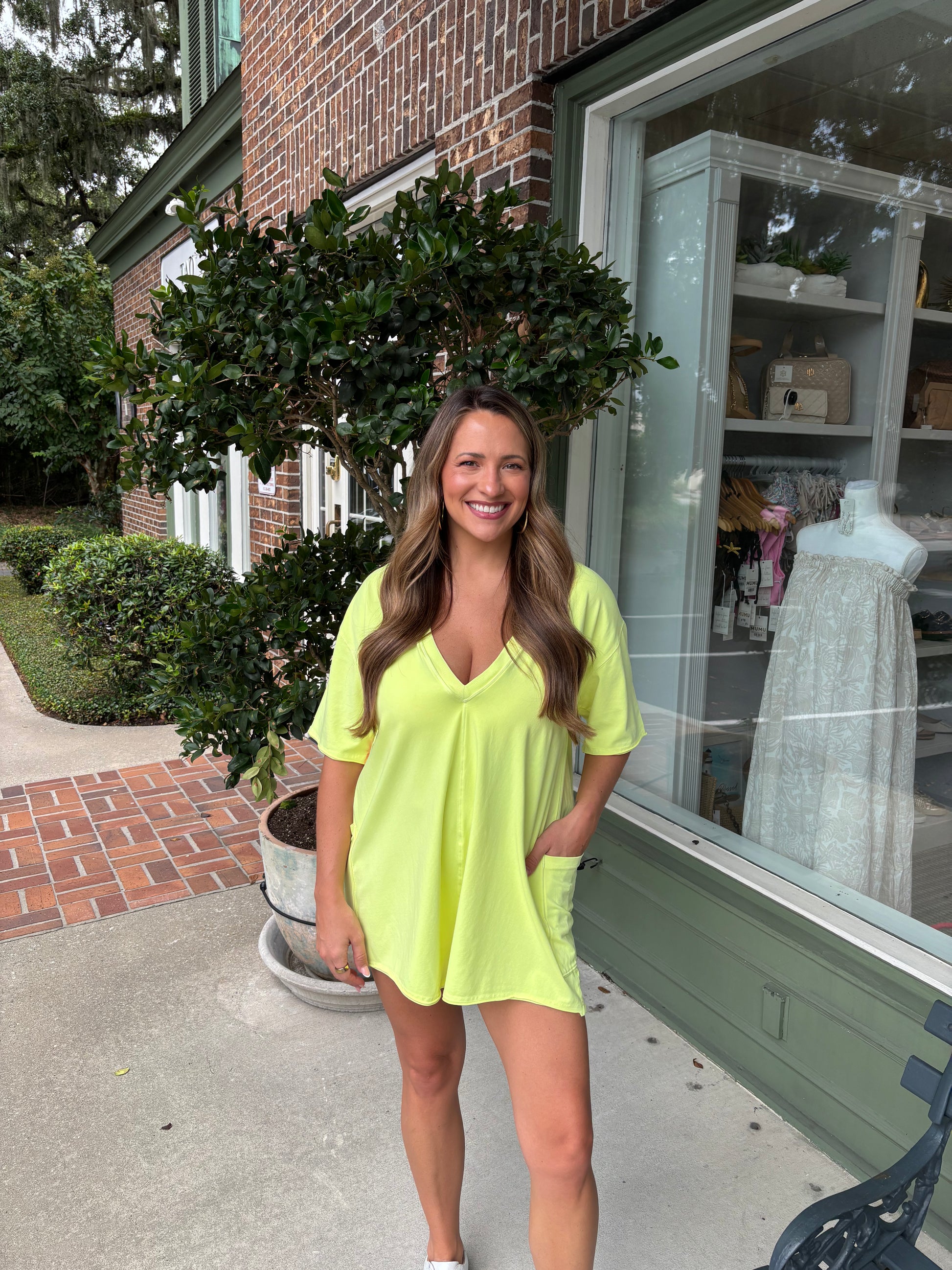Woman in a bright yellow dress standing outside a store with brick and greenery in the background
