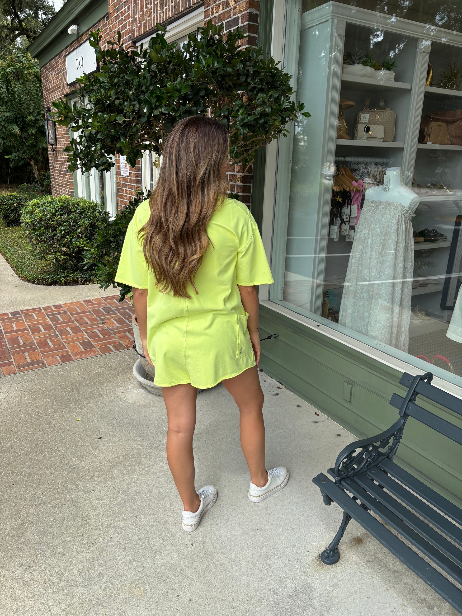 Person wearing a bright yellow outfit standing outside a store with a bench and window display.