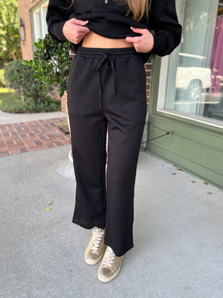 Person wearing black high-waisted pants and a cropped black top outdoors.