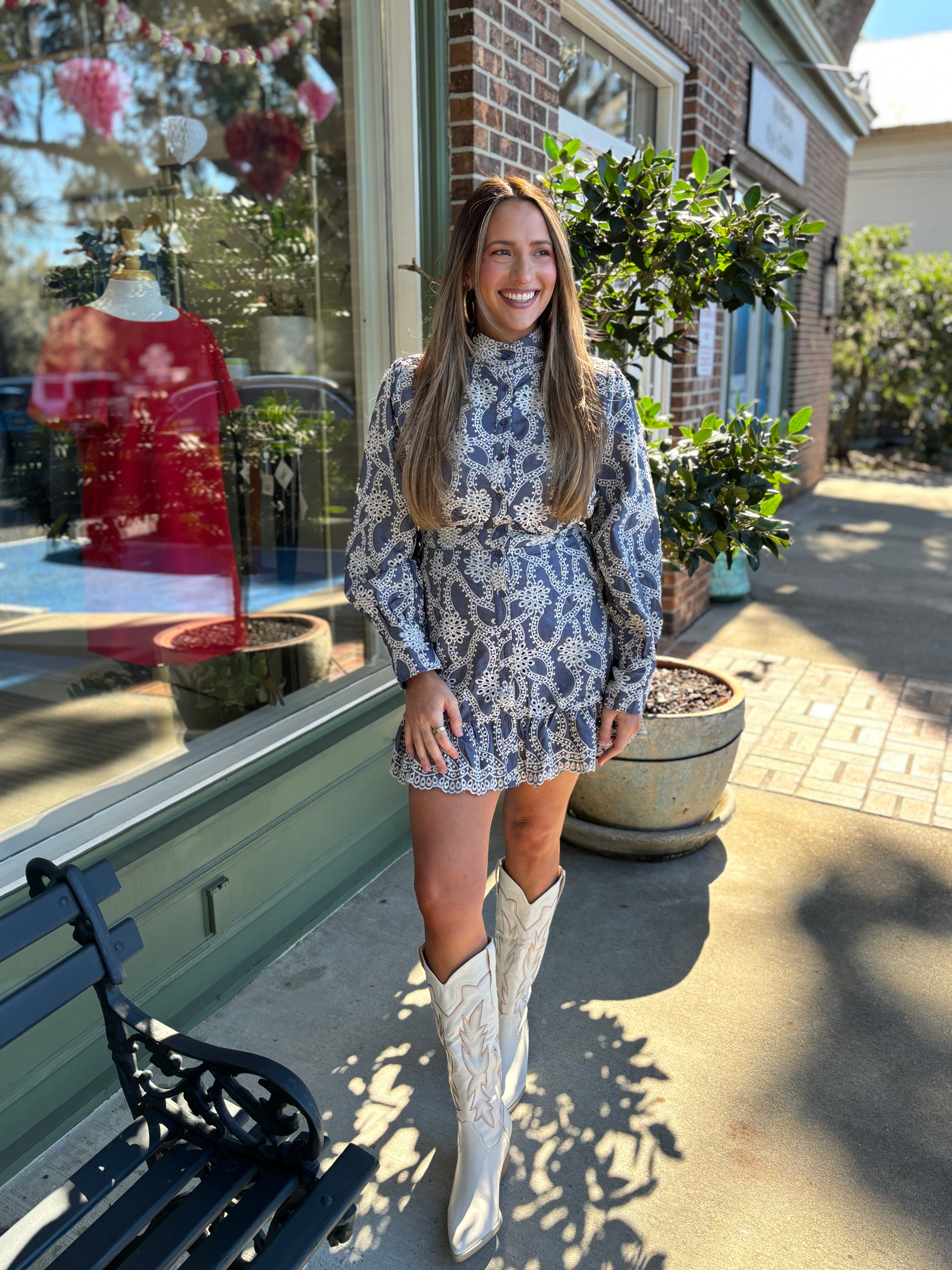 Woman in a eyelet blue dress and white boots standing outside a store 