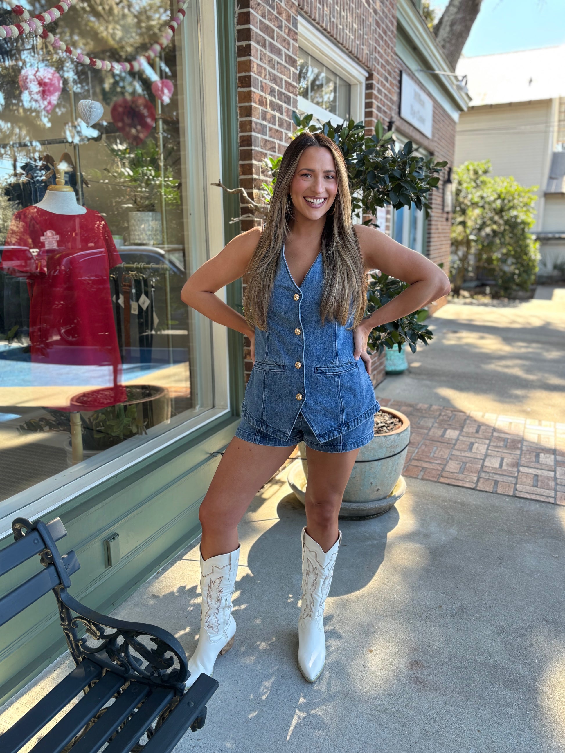 Woman in a denim romper and white cowboy boots standing in front of a store window.